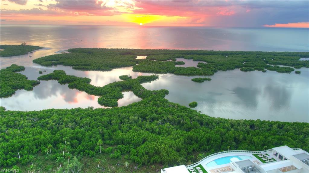 13925 Old Coast Road, Unit 1003 Naples, FL 34110 - Photo 29 of 33 Aerial view at dusk of a water view, a view of trees, and view of pool area