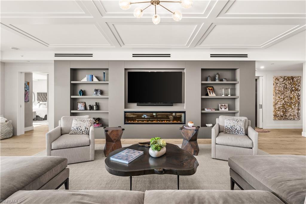 13925 Old Coast Road, Unit 1003 Naples, FL 34110 - Photo 4 of 33 Living room featuring light wood-style floors, built in shelves, a glass covered fireplace, a chandelier, and coffered ceiling