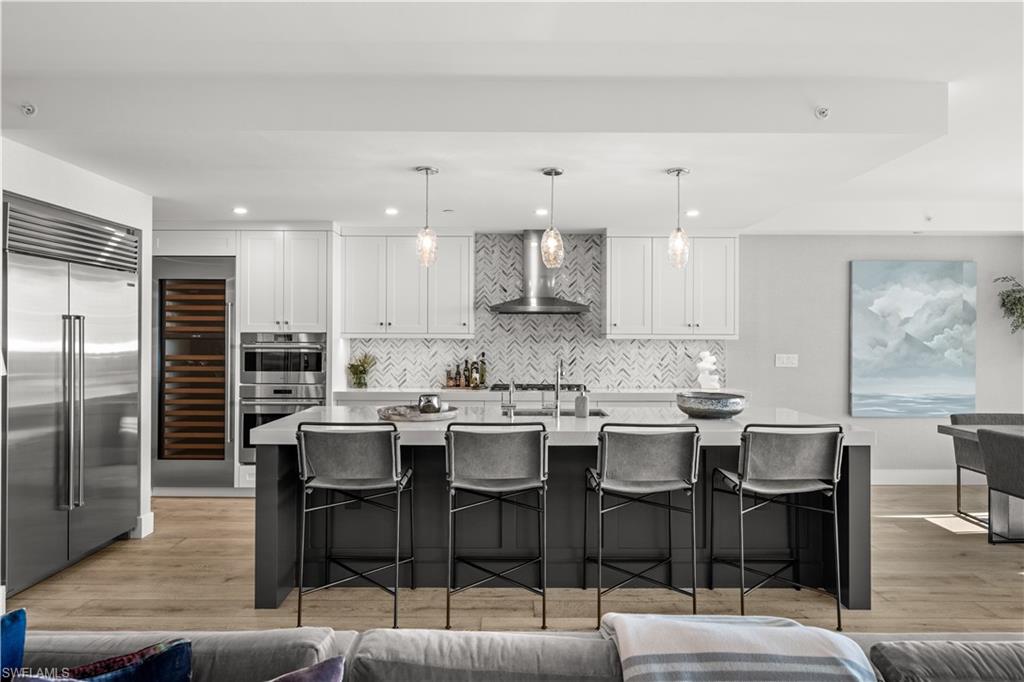 13925 Old Coast Road, Unit 1003 Naples, FL 34110 - Photo 7 of 33 Two tone kitchen featuring dual tone cabinets, a breakfast bar area, light wood-type flooring, stainless steel appliances, and wine cooler