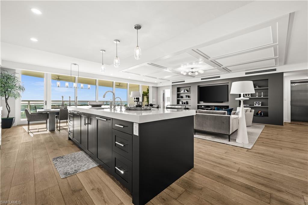 13925 Old Coast Road, Unit 1003 Naples, FL 34110 - Photo 8 of 33 Kitchen with dark cabinetry, light wood-style flooring, a center island with sink, and decorative light fixtures