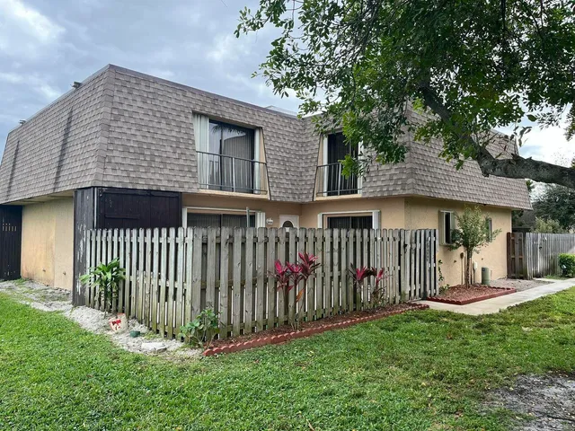 a view of a brick house with a small yard and a large tree