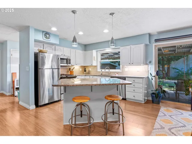 a kitchen with stainless steel appliances a refrigerator a stove a sink dishwasher and white cabinets with wooden floor