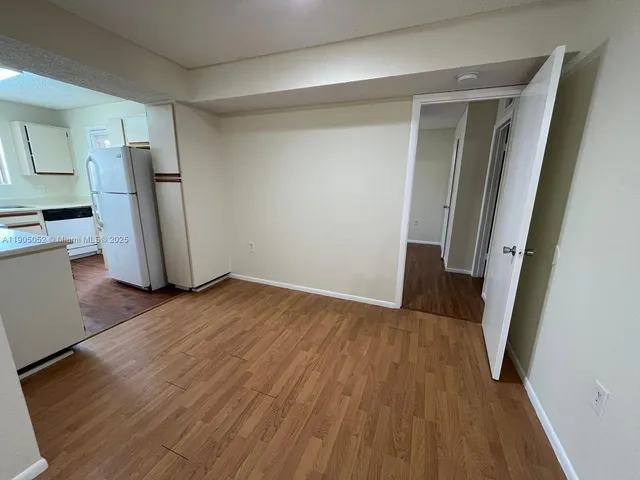 an empty room with wooden floor and a refrigerator