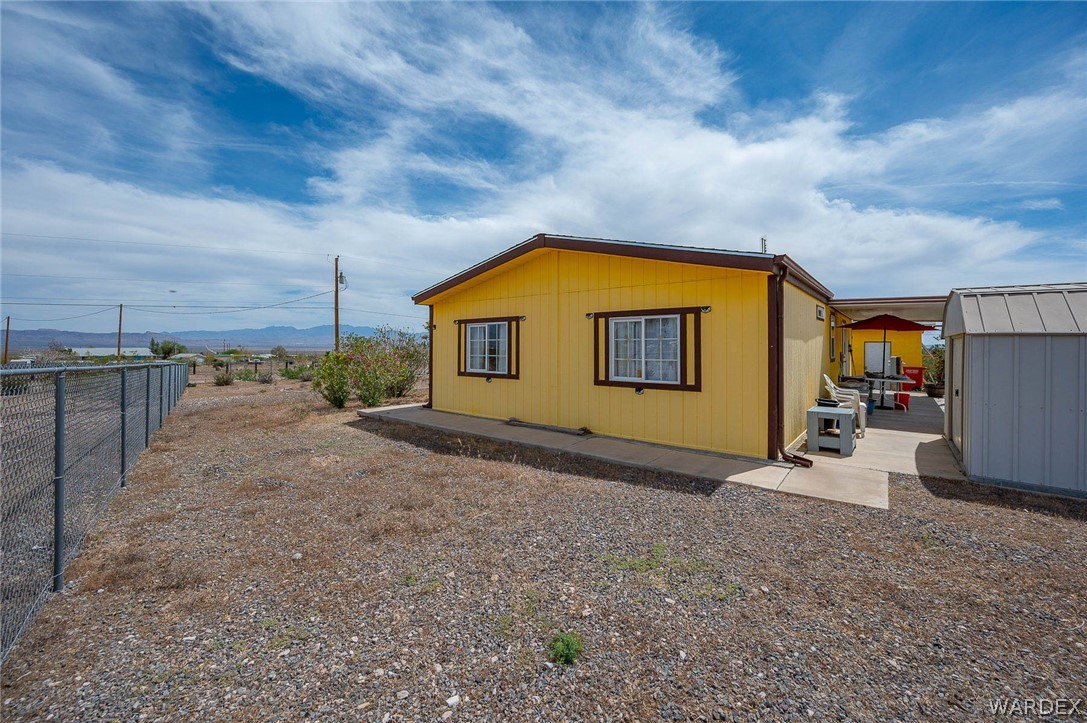 2465 Egar Road Golden Valley, AZ 86413 - Photo 50 of 98 The property features a yellow exterior with brown trim, a concrete patio area, and a separate shed for storage
