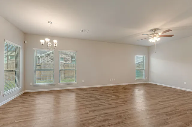 an empty room with wooden floor chandelier fan and windows