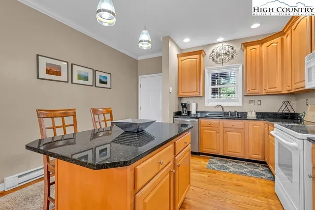 a kitchen with stainless steel appliances granite countertop a refrigerator a sink a stove a dining table and chairs with wooden floor