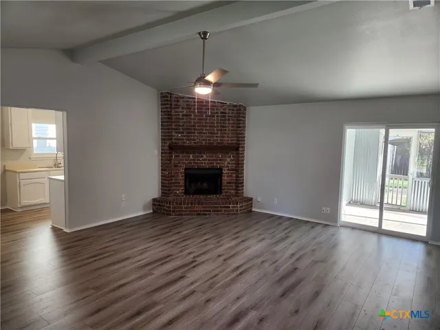a view of an empty room with wooden floor fireplace and a window