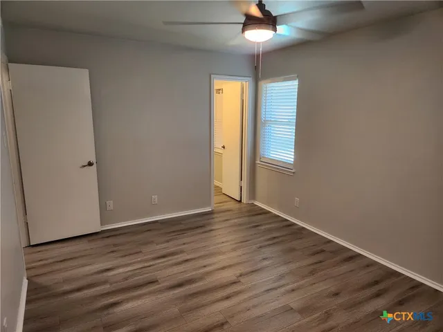 an empty room with wooden floor chandelier fan and windows