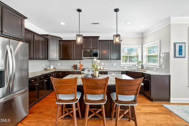 a kitchen with stainless steel appliances granite countertop a sink a stove a refrigerator cabinets a dining table and chairs