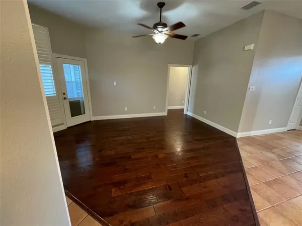 an empty room with wooden floor chandelier fan and windows