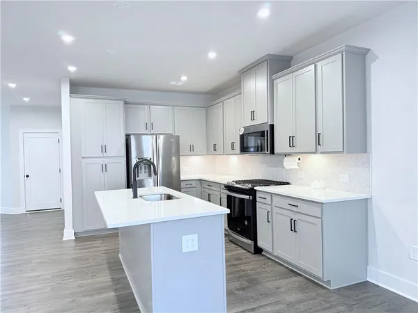 a large kitchen with stainless steel appliances kitchen island a sink dishwasher a stove and a refrigerator with wooden floor