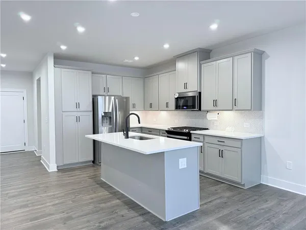 a kitchen with stainless steel appliances granite countertop a stove top oven a refrigerator a sink and white cabinets with wooden floor