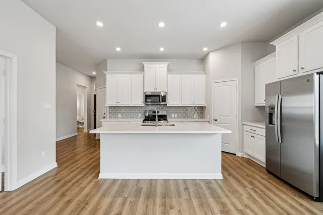 a kitchen with stainless steel appliances granite countertop a sink a stove a refrigerator and white cabinets with wooden floor