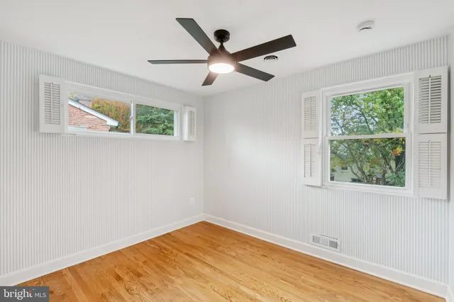 a view of an empty room with wooden floor and a ceiling fan