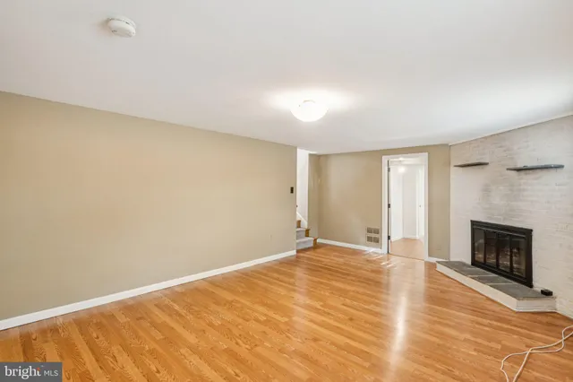 a view of an empty room with wooden floor fireplace and a window