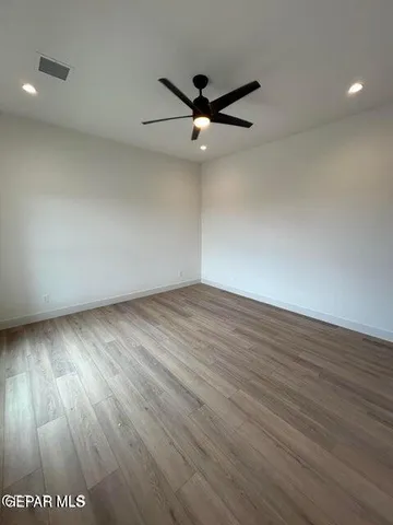 a view of an empty room with wooden floor and a ceiling fan