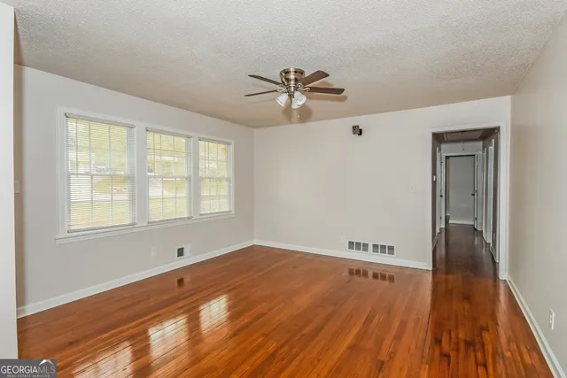 an empty room with wooden floor fan and windows