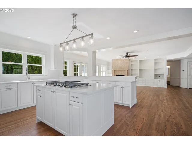 a kitchen with granite countertop a stove a sink a refrigerator and white cabinets with wooden floor