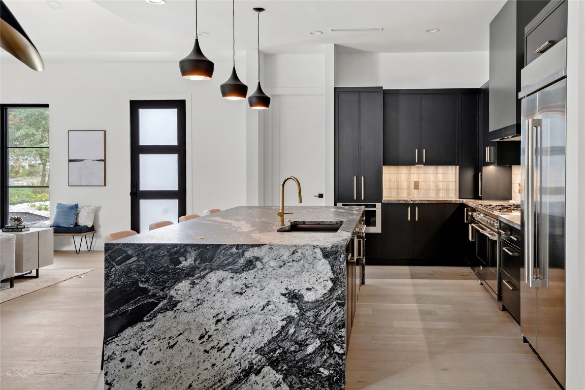 1803 Palo Duro Road Austin, TX 78757 - Photo 9 of 34 Kitchen featuring light stone counters, backsplash, dark cabinetry, hanging light fixtures, and premium appliances