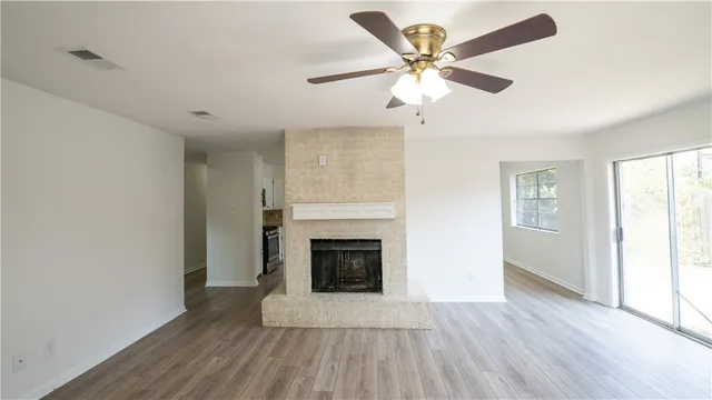 an empty room with wooden floor a ceiling fan and fireplace