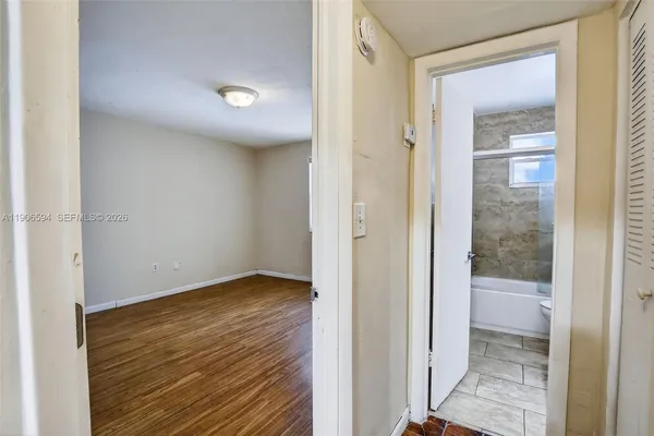 a view of an empty room with wooden floor and a bathroom