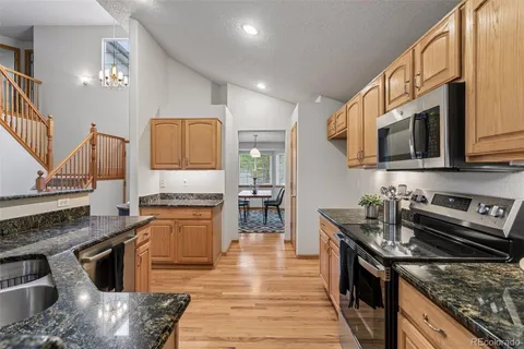a kitchen with stainless steel appliances granite countertop a stove top oven a sink dishwasher a dining table and chairs with wooden floor