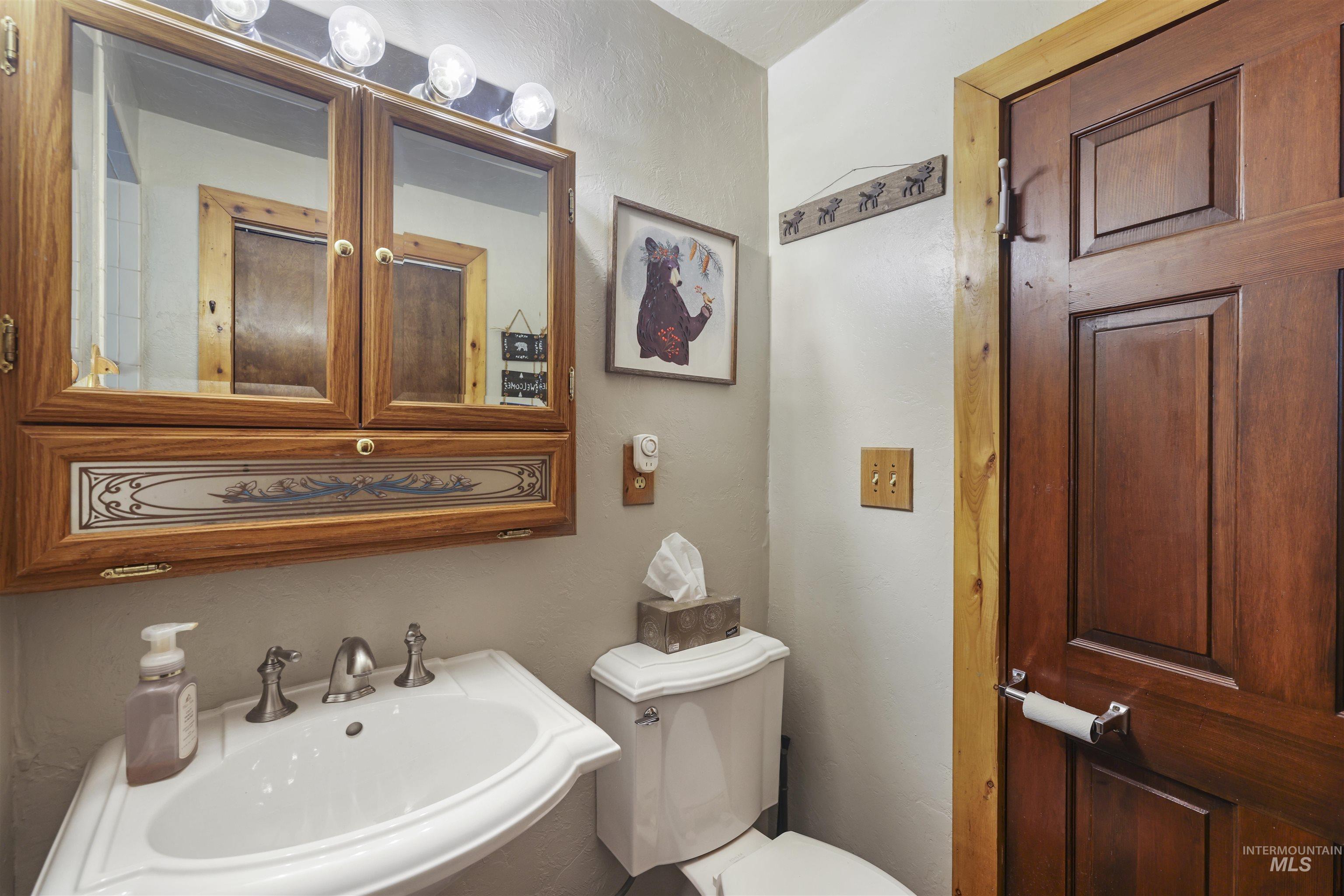 224 Dakota Road Mountain Home, ID 83647 - Photo 15 of 50 Bathroom featuring a white pedestal sink with a dual-handle faucet, a vanity mirror cabinet with decorative trim, a white toilet, and a solid wood panel door with a wood frame