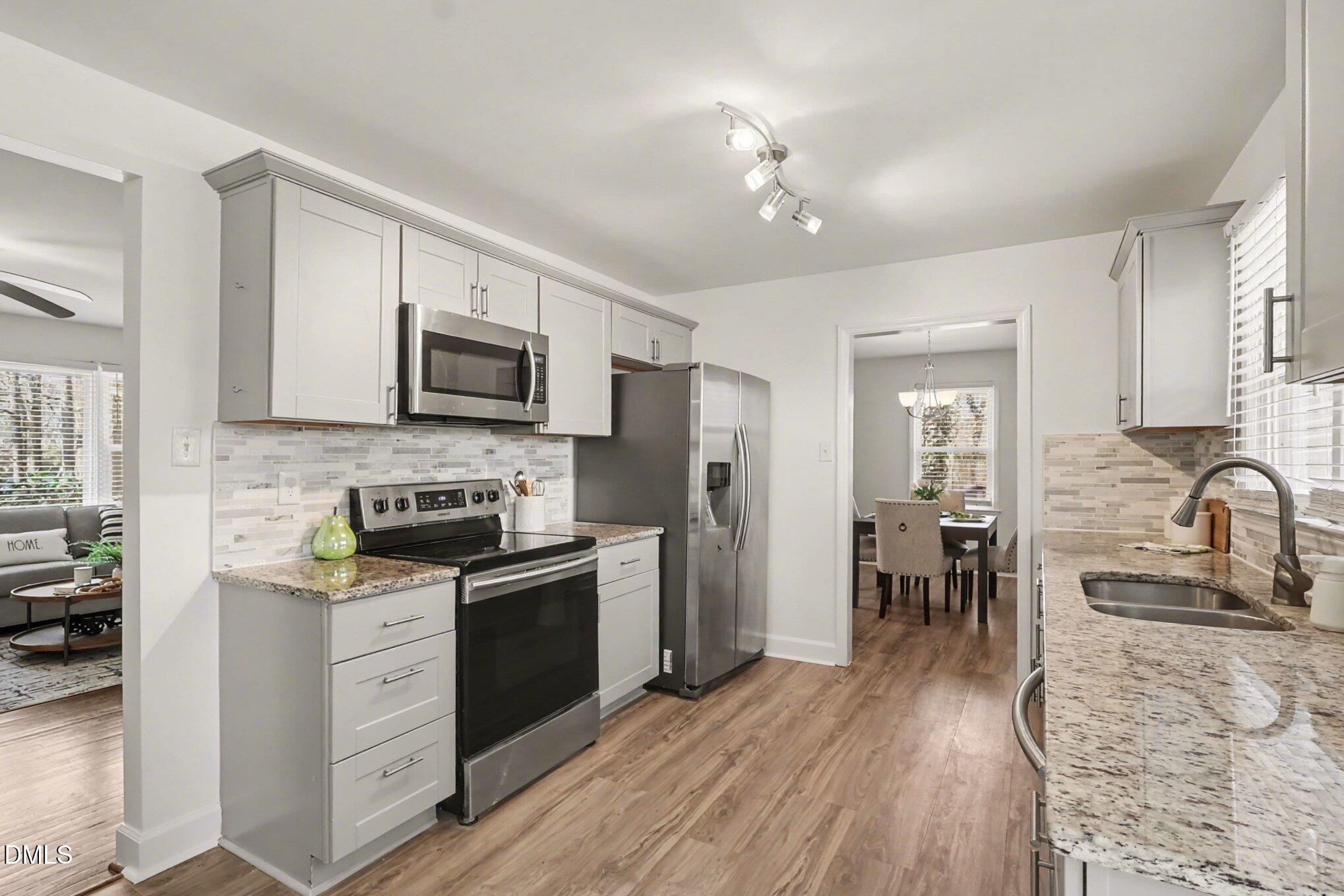 3043 Creech Road Garner, NC 27529 - Photo 7 of 38 a kitchen with granite countertop a stove top oven a sink dishwasher a dining table and chairs with wooden floor