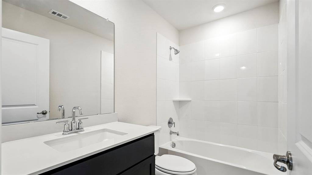 4159 Waldron Trail Forney, TX 75126 - Photo 18 of 19 The bathroom features a modern vanity with a white countertop and dark cabinetry, a spacious mirror, and a clean white tiled shower and bathtub combination