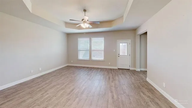 an empty room with wooden floor chandelier fan and windows
