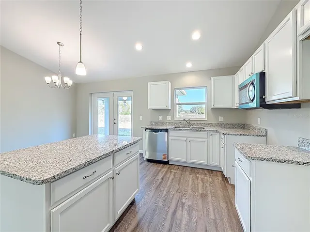 a kitchen with granite countertop white cabinets a sink dishwasher and a stove with wooden floor