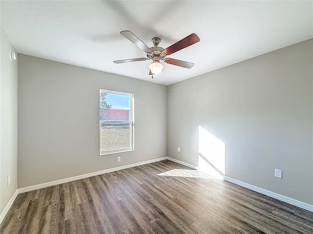 an empty room with wooden floor ceiling fan and windows