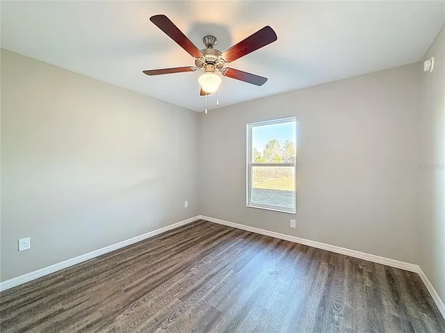 an empty room with wooden floor window and ceiling fan