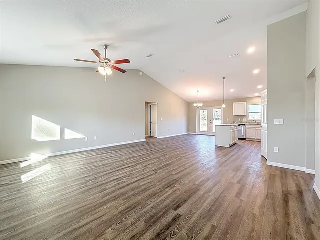 a view of an empty room and kitchen with wooden floor