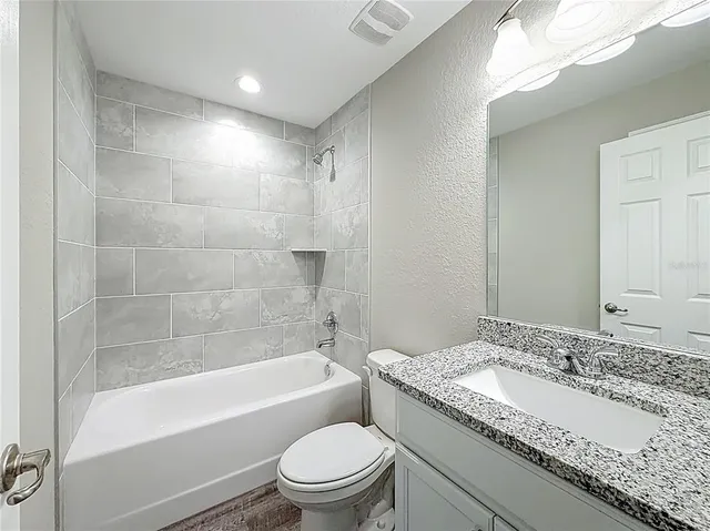 a bathroom with a granite countertop sink a toilet and bathtub