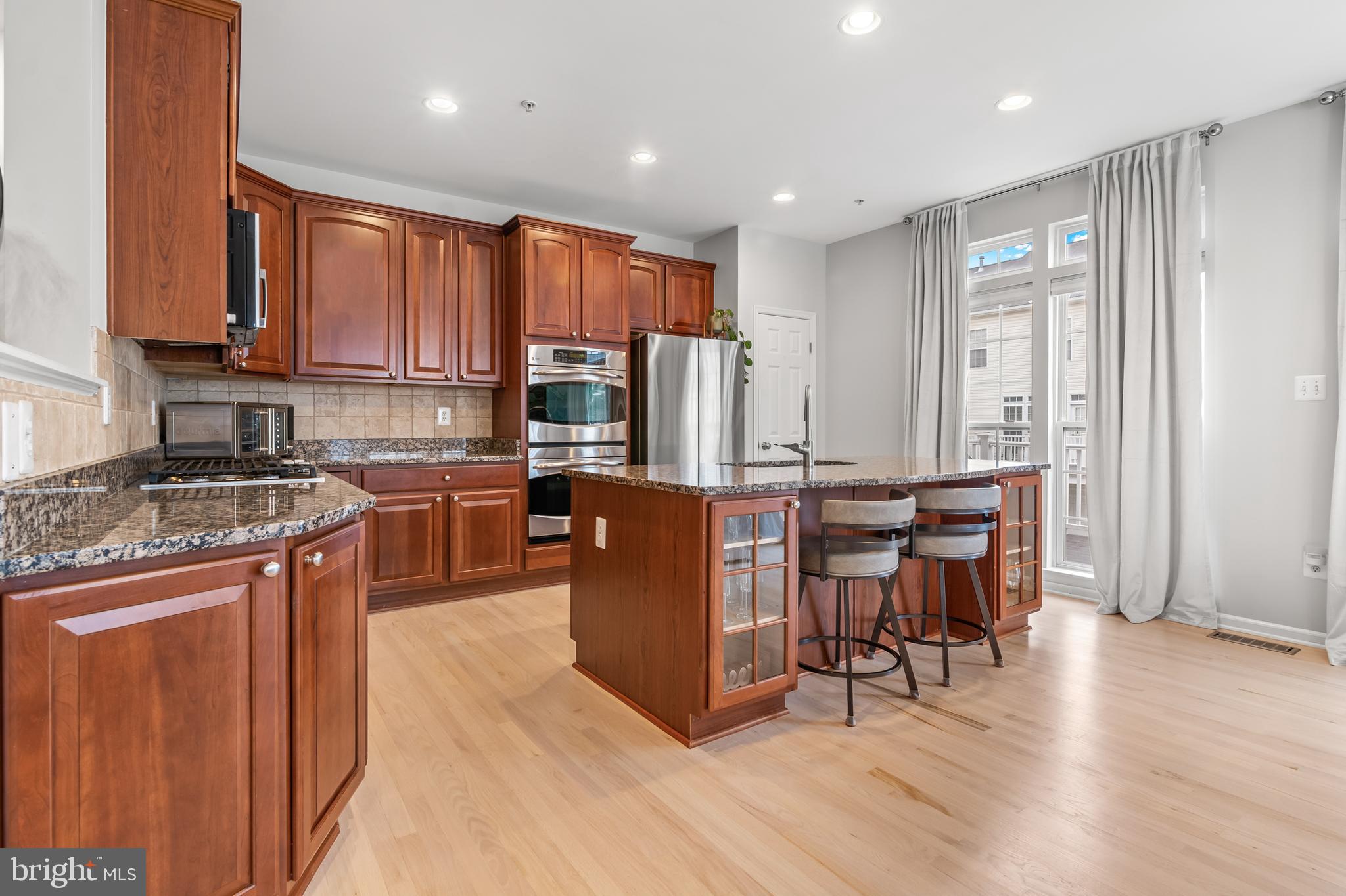 1750 Theale Way Hanover, MD 21076 - Photo 15 of 42 a kitchen with stainless steel appliances granite countertop a refrigerator a stove top oven and a dining table with wooden floor