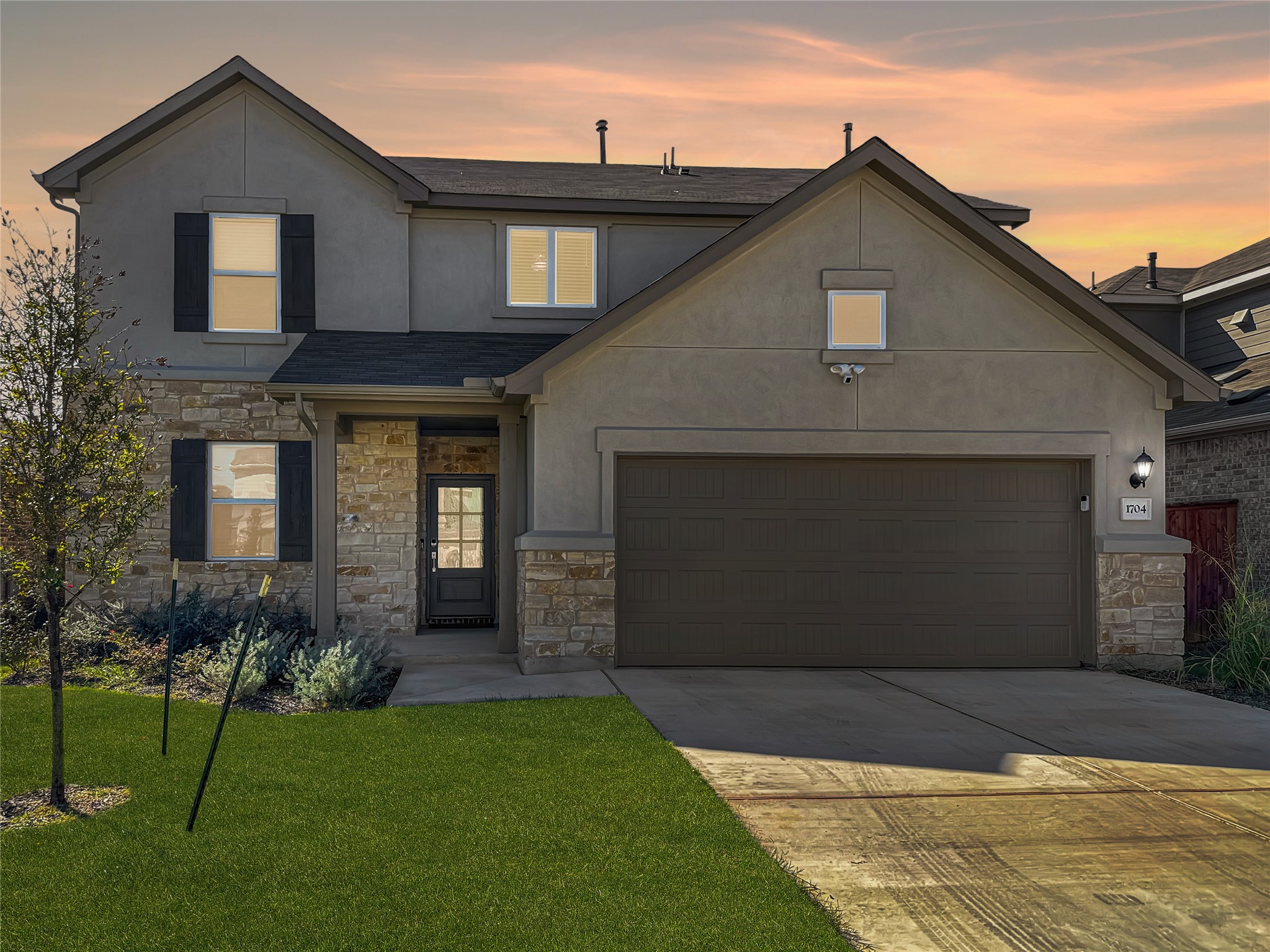 View of front of house with stone siding, concrete driveway, a front yard, stucco siding, and a garage