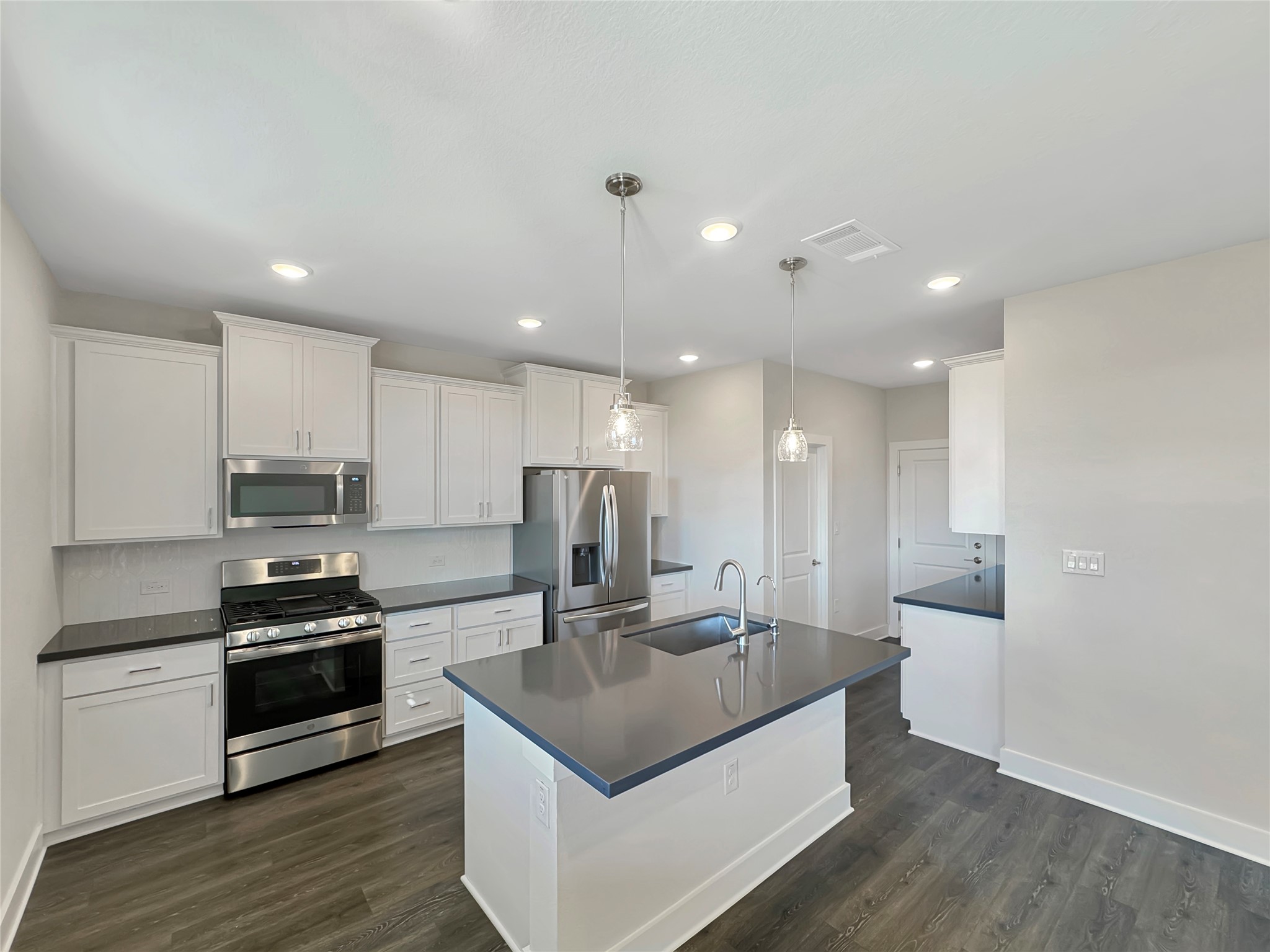 1704 Carvin Way Pflugerville, TX 78660 - Photo 10 of 30 Kitchen with stainless steel appliances, dark countertops, dark wood-type flooring, white cabinetry, and an island with sink