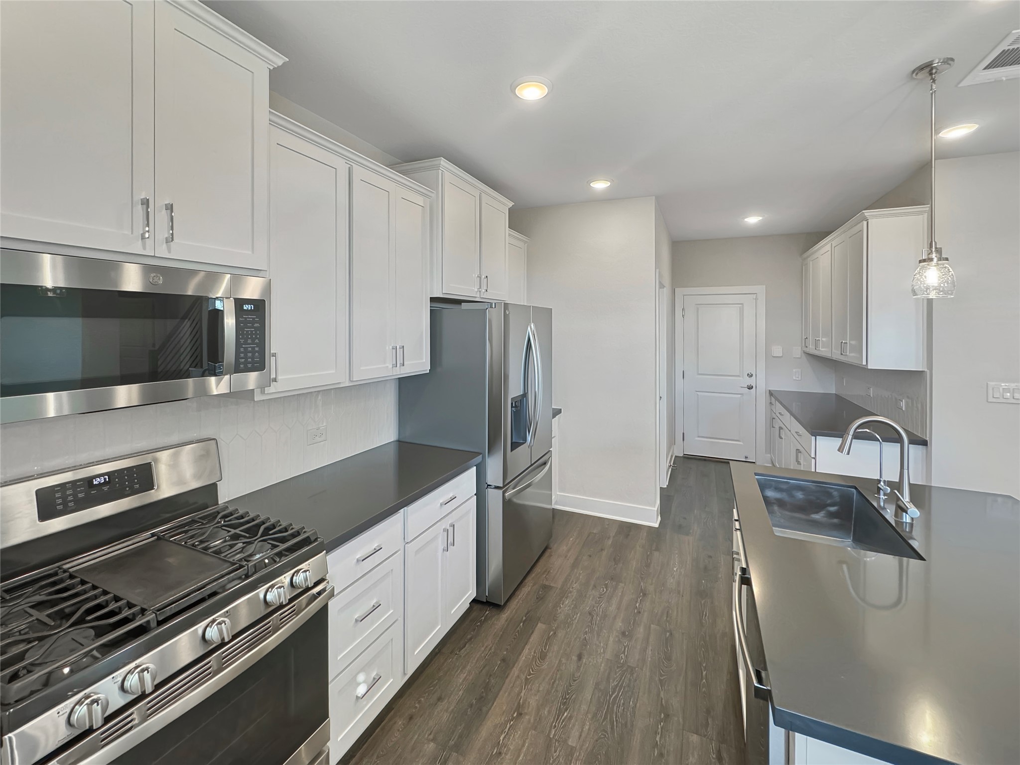 1704 Carvin Way Pflugerville, TX 78660 - Photo 9 of 30 Kitchen with stainless steel appliances, white cabinetry, dark countertops, and decorative light fixtures