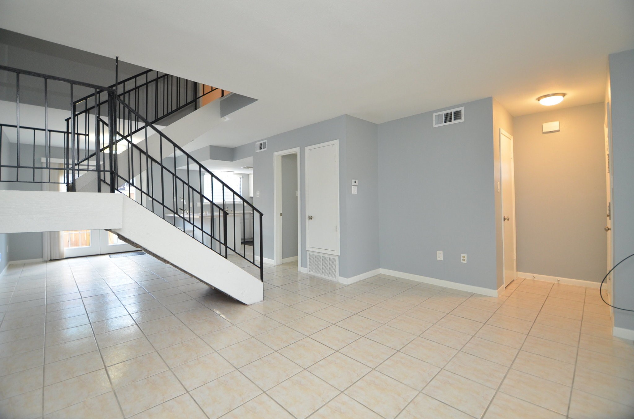 10018 Knoboak Drive, Unit 13 Houston, TX 77080 - Photo 21 of 37 This spacious living area features light tile flooring and a modern open staircase with metal railings. The neutral gray walls complement the bright, airy feel, enhanced by natural light from large windows and a glass door leading outside. Ideal for contemporary living.