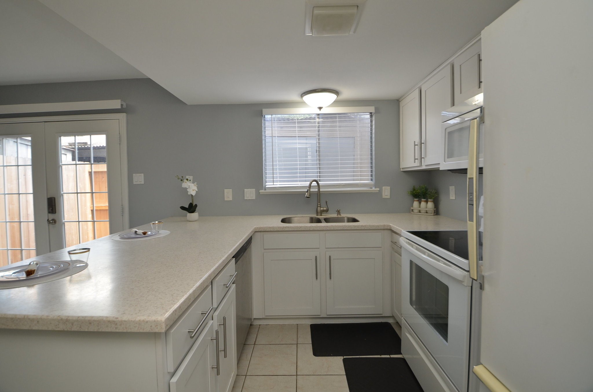 10018 Knoboak Drive, Unit 13 Houston, TX 77080 - Photo 4 of 37 This kitchen features a clean, modern design with white cabinetry, ample countertop space, and a double sink. It includes an oven, stove, and a large window for natural light. French doors lead to the outside, enhancing the open feel.
