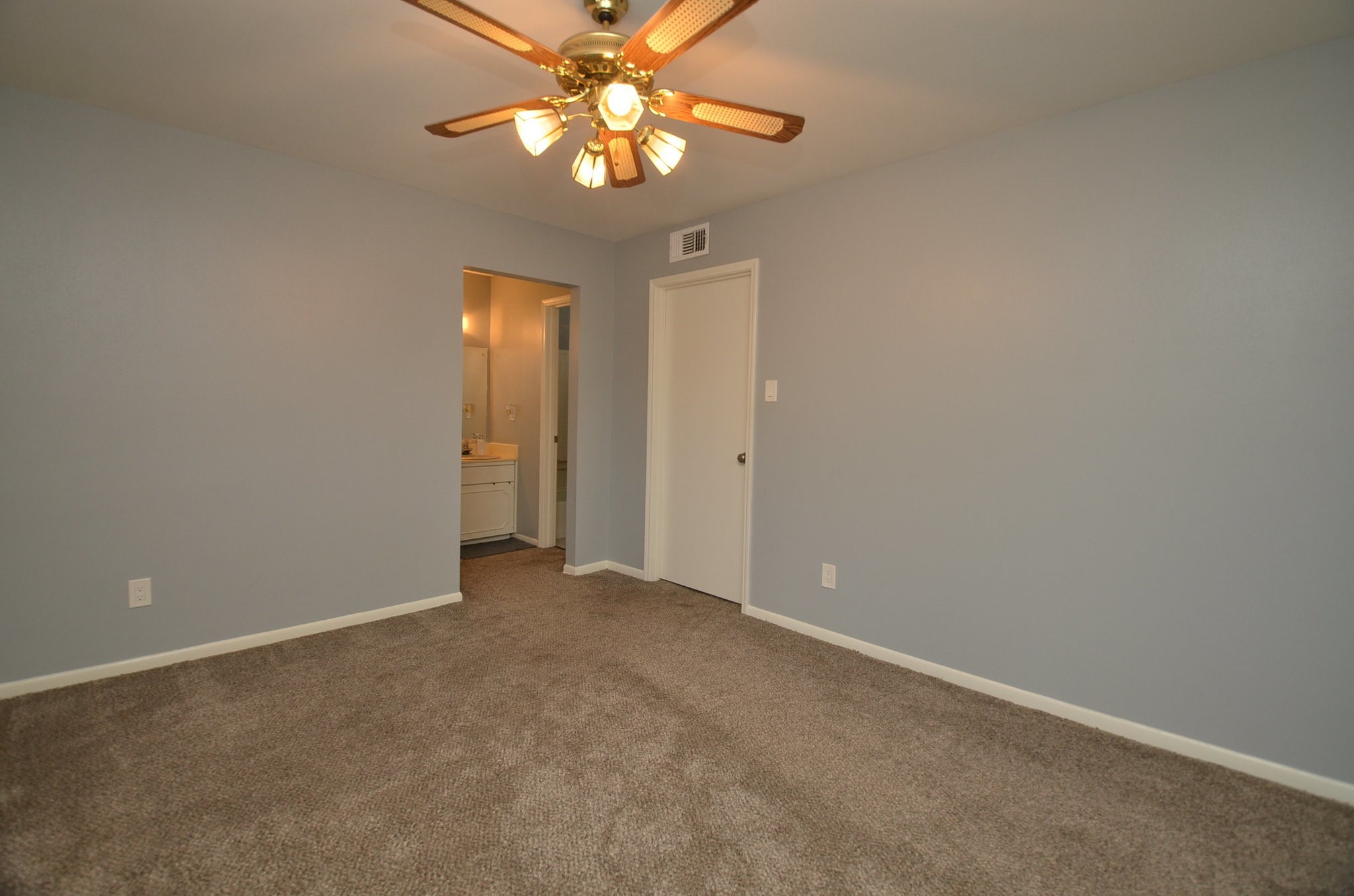 10018 Knoboak Drive, Unit 13 Houston, TX 77080 - Photo 8 of 37 This photo shows a cozy bedroom with soft gray walls and carpeted flooring. It features a ceiling fan with lights and an open doorway leading to a bathroom area. Perfect for a comfortable and functional living space.