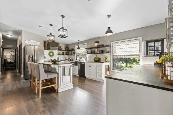 a kitchen with stainless steel appliances granite countertop a stove a refrigerator a sink dishwasher a dining table and chairs with wooden floor
