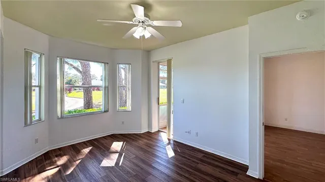 an empty room with wooden floor chandelier fan and windows