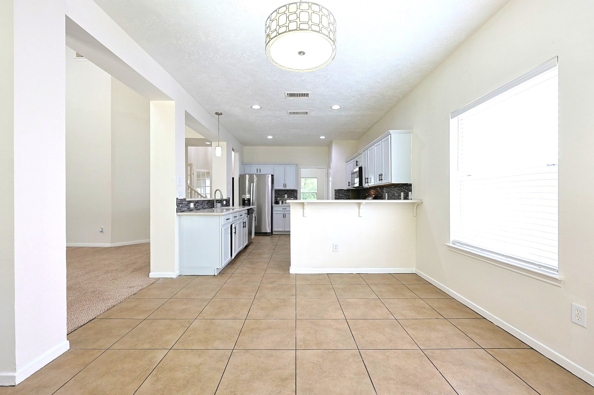 23019 Eastgate Village Drive Spring, TX 77373 - Photo 15 of 46 This photo showcases a bright, open kitchen and dining area with tile flooring and neutral walls. The kitchen features modern appliances, a spacious countertop, and bar seating. Natural light fills the space through a large window, creating a welcoming atmosphere.