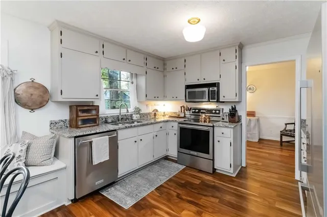 a kitchen with stainless steel appliances granite countertop a stove top oven a sink dishwasher a dining table and chairs cabinets with wooden floor