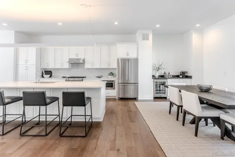 a kitchen with stainless steel appliances kitchen island granite countertop a dining table chairs and a refrigerator