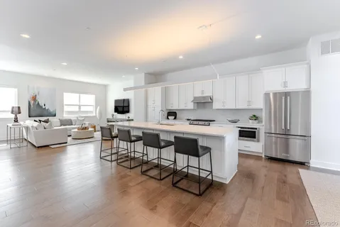 a kitchen with a refrigerator a white cabinets and couches with wooden floor