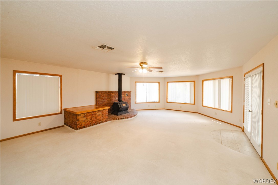 2100 East Valley View Road Kingman, AZ 86409 - Photo 14 of 53 Spacious room featuring a brick fireplace with a wood-burning stove, multiple large windows with horizontal blinds, a ceiling fan, and a light-colored carpeted floor