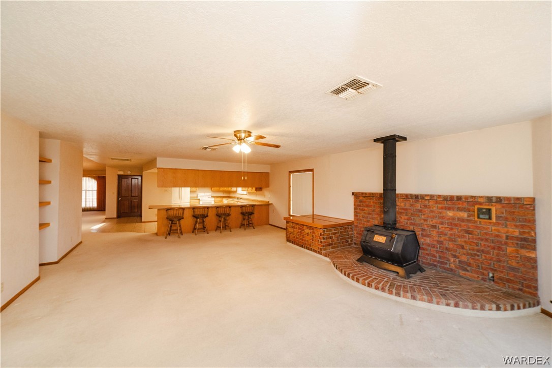 2100 East Valley View Road Kingman, AZ 86409 - Photo 18 of 53 Open-concept living space featuring a brick-surround wood-burning stove, built-in shelving, wood-finish flooring, and a kitchen bar with overhead cabinetry